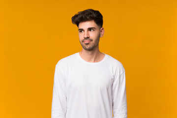 Young man over isolated orange background making doubts gesture looking side