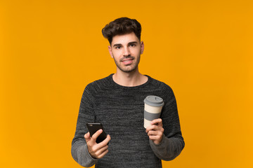 Young man over isolated background holding coffee to take away and a mobile