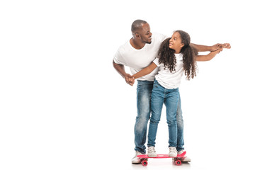 Cheerful African American father supporting daughter skateboarding on white background - Powered by Adobe