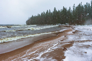 frozen sandy shore under snowfall with the forest on the background