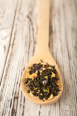 Loose tea in a wooden spoon close-up. Macro tea on a spoon on a textural wooden white table and copy space. Top view.