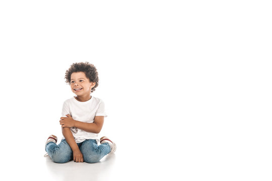 Cheerful African American boy looking away while sitting on white background