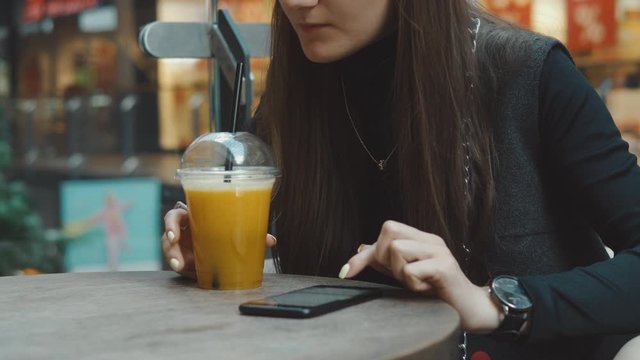 Young woman browsing on smartphone in cafe on wooden table, drinking juce. Businesswoman typing on mobile phone. 4K UHD