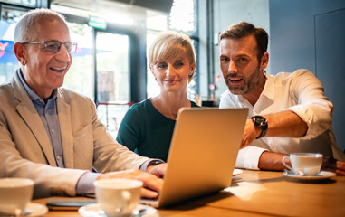 Business people looking at laptop at cafe and discussing