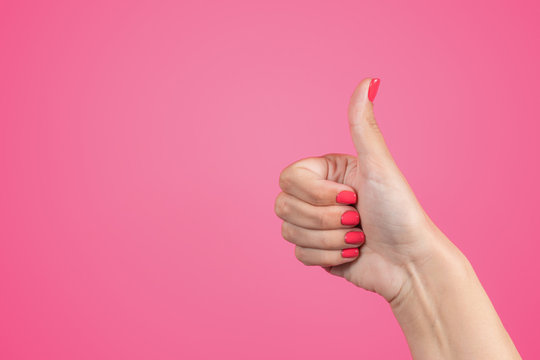 Closeup of female hand with thumb up isolated on bright pink background. Woman shows like symbol gesture. Manicured nails painted with beautiful modern pink gel polish. Horizontal color photography.