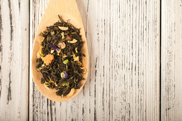 Loose tea in a wooden spoon close-up. Macro tea on a spoon on a textural wooden white table and copy space. Top view.