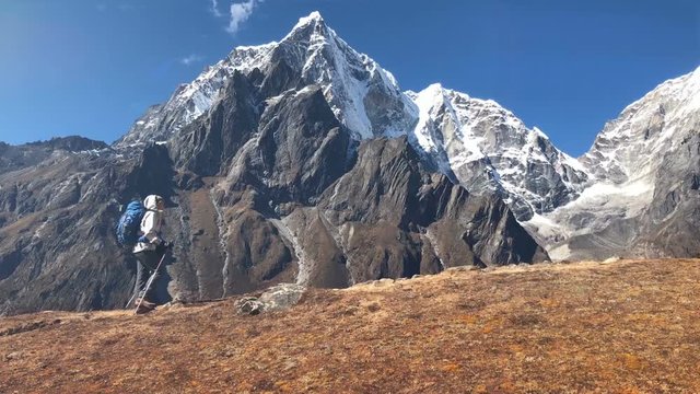 Young hiker backpacker female using trekking poles hiking during high altitude Everest Base Camp (EBC) route with snow Tobuche 6495m mountain peak on background. Extremly Active vacations concept 