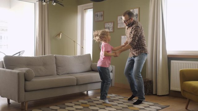 Young Father and Her Daughter Playing in Living Room. Funny Happy Family Father and Daughter are Dancing hold hands and jump at Home. Love Lifestyle Home. Slow Motion.