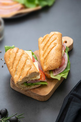 Sandwich with baguette bread, ham, lettuce, tomatoe over dark background. Breakfast or fast food.