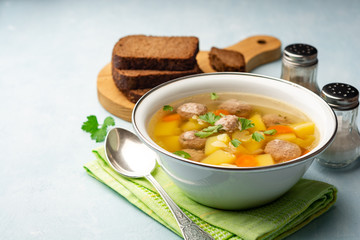 Soup with meatballs and vegetables in bowl on concrete background. Selective focus.