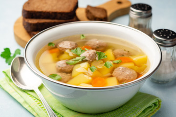 Soup with meatballs and vegetables in bowl on concrete background. Selective focus.