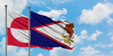 Greenland and American Samoa flag waving in the wind against white cloudy blue sky together....
