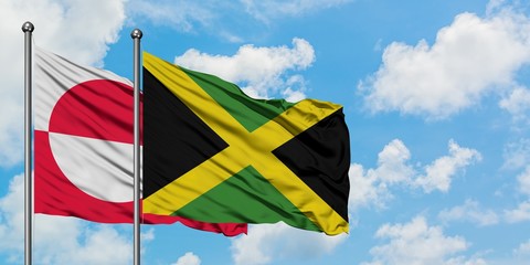 Greenland and Jamaica flag waving in the wind against white cloudy blue sky together. Diplomacy concept, international relations.