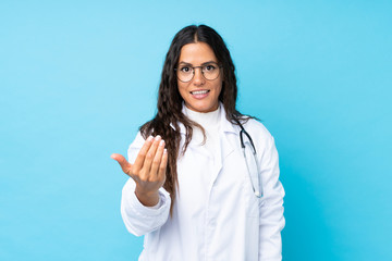 Young doctor woman over isolated blue background inviting to come