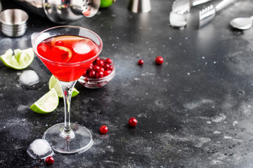 Cosmopolitan cocktail with vodka, liqueur, cranberry juice, lime, ice and orange zest, gray bar...