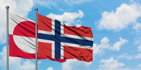 Greenland and Norway flag waving in the wind against white cloudy blue sky together. Diplomacy concept, international relations.