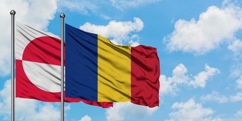 Greenland and Romania flag waving in the wind against white cloudy blue sky together. Diplomacy...