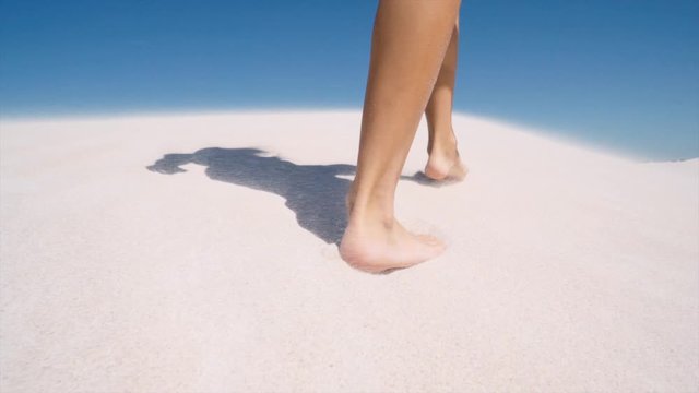 Close-up slow-motion shot of following a person walking bare feet on a sand dune during mid-day.