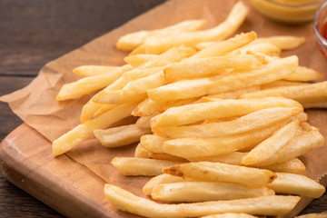 Golden yummy deep French fries on kraft baking sheet paper and serving tray to eat with ketchup and yellow mustard, close up, lifestyle.