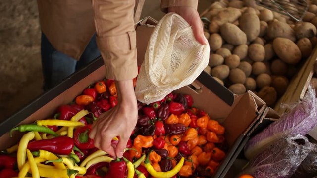 Close-up female hands pick hot pepper in a reusable fabric bag. Shopping in the market, ecological packaging
