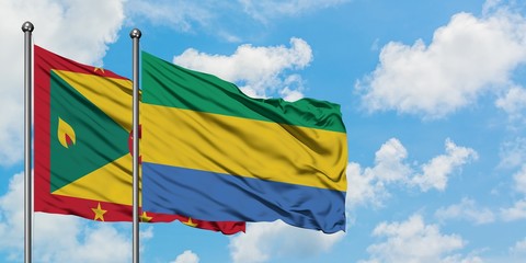Grenada and Gabon flag waving in the wind against white cloudy blue sky together. Diplomacy...