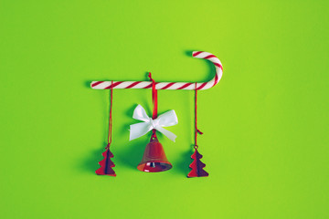 Composition of  christmas minimalism on a green background. Red Christmas tree toys and bells and candy cane.