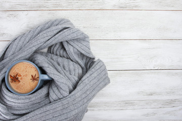 Cup of spicy coffee wrapped in grey wool scarf or plaid. Autumn or winter drink concept, Latte, cappuccino, October, November, anise