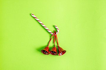 Christmas background. In the center of the green table is a Christmas cane lollipop and three red bells. Save space