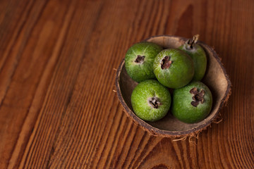 Green feijoa in a coconut shell hulf on a dark wooden background. Ripe tropical fruits, pineapple guava, raw vegan food. Low calories, rich in dietary fiber, vitamin C and B6, minerals. Copy space.