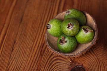 Green feijoa in a coconut shell hulf on a dark wooden background. Ripe tropical fruits, pineapple guava, raw vegan food. Low calories, rich in dietary fiber, vitamin C and B6, minerals. Copy space.