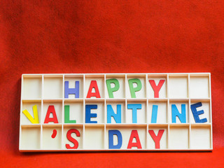 Multicolored wooden alphabets or letters of happy valentine 's day texts or words in wooden grids box on rough vivid or vibrant gradient red paper texture and background.