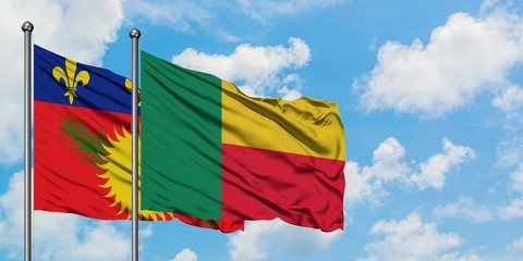 Guadeloupe and Benin flag waving in the wind against white cloudy blue sky together. Diplomacy concept, international relations.