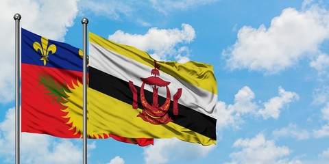 Guadeloupe and Brunei flag waving in the wind against white cloudy blue sky together. Diplomacy concept, international relations.
