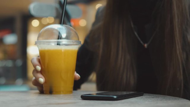 Young woman browsing on smartphone in cafe on wooden table, drinking juce. Businesswoman typing on mobile phone. 4K UHD