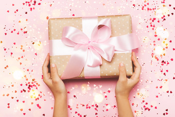 Girl's hands holding gift in kraft box with lush ribbon. Pink colors. Present for St. Valentine's day, Mother's Day, birthday, New Year, Christmas, holidays. Flat lay