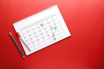 Planning calendar with pins and pen, on a red background with place for text. Important date. Place for text. Planning concept.