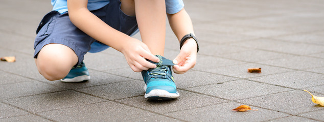 Banner of a young healthy asian schoolboy putting on his running shoes by himself in the playground. Life skills, Self-care, , Comfortable kids shoes, Sport day, Outdoor fun, Get ready concept.