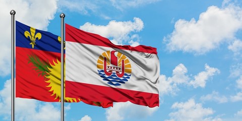 Guadeloupe and French Polynesia flag waving in the wind against white cloudy blue sky together. Diplomacy concept, international relations.