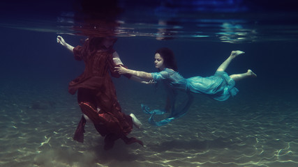 Fototapeta na wymiar Two girls in dresses play underwater