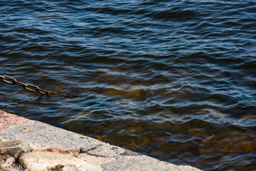 Rust metal chain goes under blue water on a dock