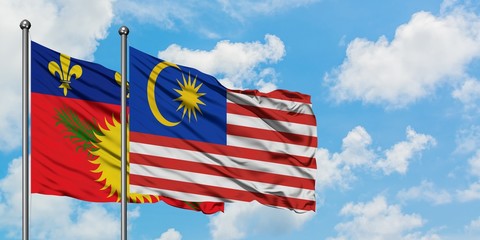 Guadeloupe and Malaysia flag waving in the wind against white cloudy blue sky together. Diplomacy concept, international relations.