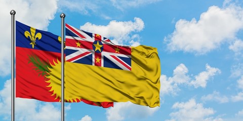 Guadeloupe and Niue flag waving in the wind against white cloudy blue sky together. Diplomacy concept, international relations.