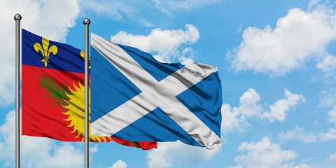 Guadeloupe and Scotland flag waving in the wind against white cloudy blue sky together. Diplomacy concept, international relations.