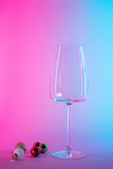 empty glass of wine with christmas tree ball decorations in pink and blue neon gradient light