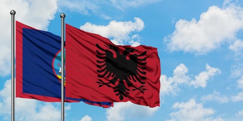 Guam and Albania flag waving in the wind against white cloudy blue sky together. Diplomacy concept, international relations.