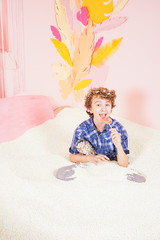 teen boy in the pool with foam soft small white balls. person engaged in relaxation therapy. caucasian kid with colorful lollipop on the stick on pink background.