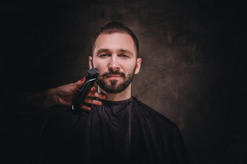 Young attractive brunette is visiting a barbershop for a care about his beard.