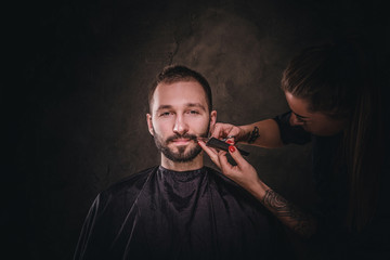 Portrait of handsome male at elite barbershop, he gets facial hair care from female.