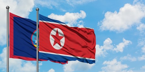 Guam and North Korea flag waving in the wind against white cloudy blue sky together. Diplomacy concept, international relations.