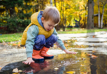 toddler boy sitting in puddle in rubber rain boots